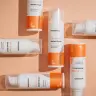 Verschillende flesjes Hemptouch - Skin Perfection - CBD Azelaic Serum voor gezicht (30ml) staan op een perzikkleurig oppervlak, met geometrische patronen van licht en schaduw. miniatuur