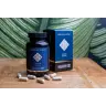Een flesje en doosje MindScopic - CLEAR FOCUS™ Capsules (50 stuks) staan op een houten oppervlak met verspreid liggende capsules en een groen bladpatroon op de achtergrond. miniatuur