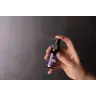 Een hand spuit een klein flesje met de tekst "MindScopic - SLEEPWELL SPRAY met melatonine (15ml)" tegen een donkere achtergrond. miniatuur