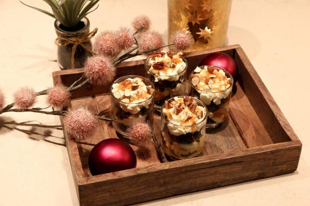 een houten dienblad met desserts erop naast een vaas met bloemen.