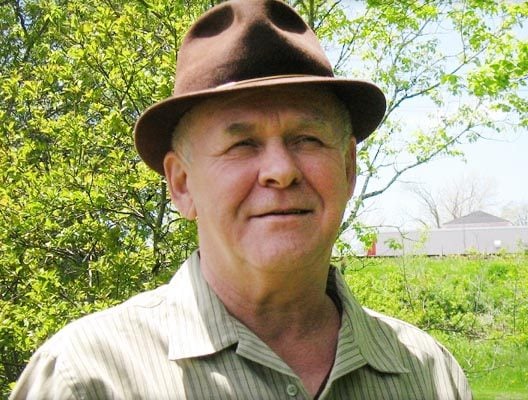 een oudere man met een hoed op in een veld.