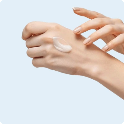 Een hand met een beetje lotion op de rug, terwijl de andere hand zich klaarmaakt om het in te wrijven, tegen een lichtblauwe achtergrond.